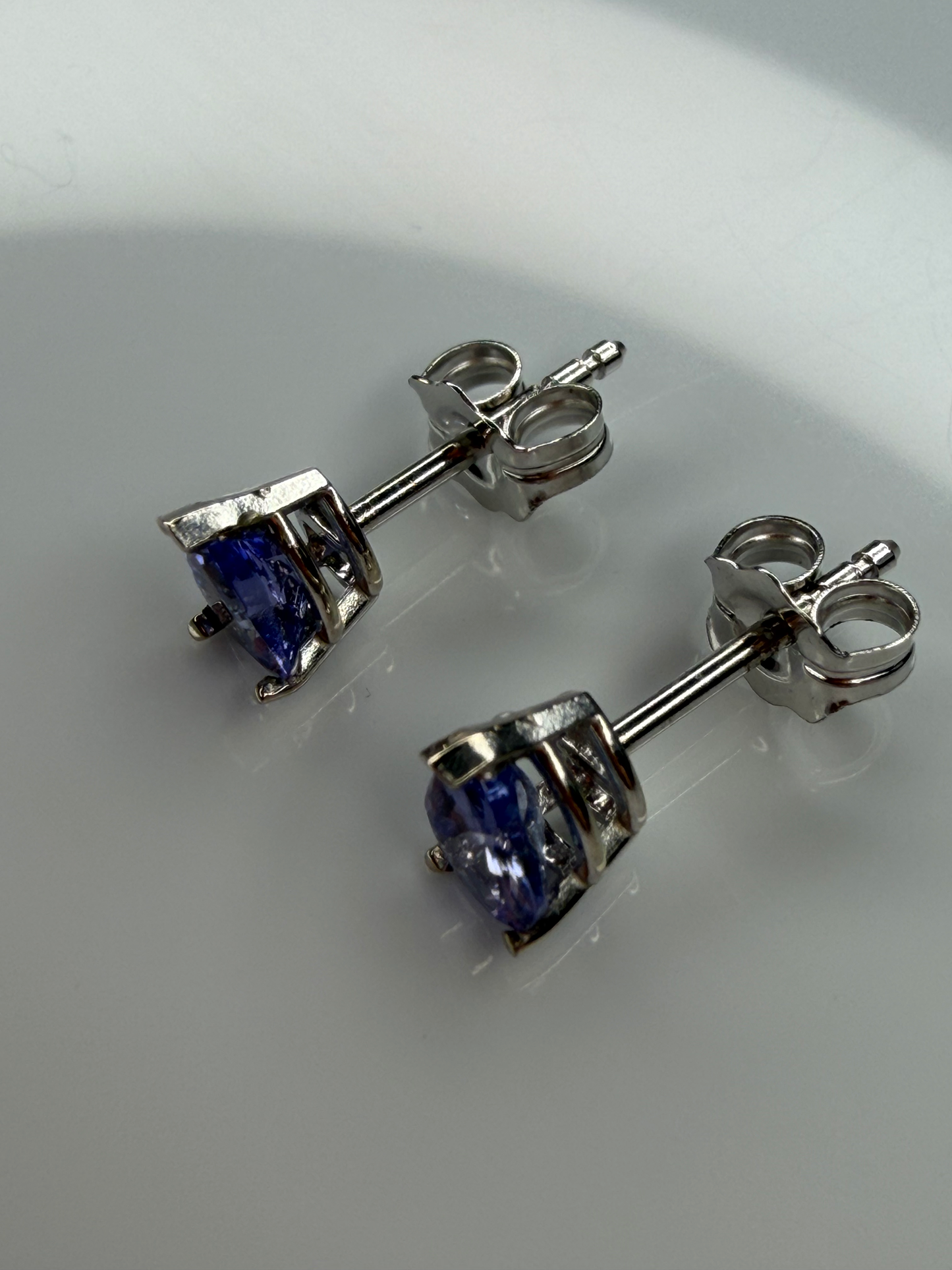 A pair of white gold stud earrings with tanzanite gemstones, shown on a light reflective surface.