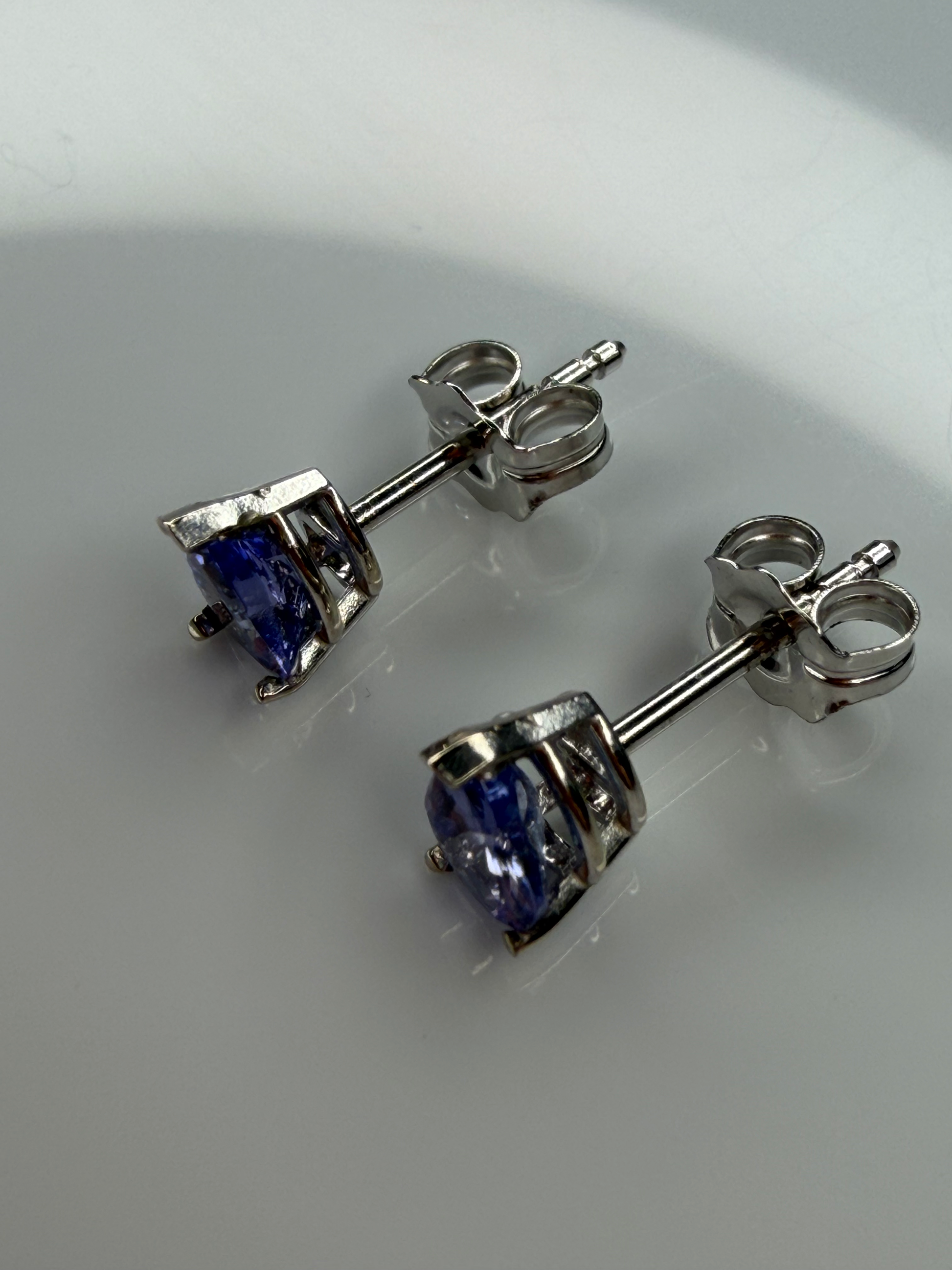 A pair of white gold stud earrings with tanzanite gemstones, shown on a light reflective surface.