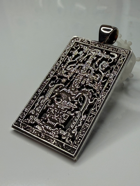 A rectangular silver-toned pendant with intricate embossed and cutout Thai script and traditional decorative motifs, displayed on a light gray background.